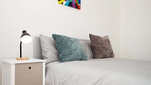 Un letto con materasso bianco, due cuscini, un comodino con una lampada e un quadro astratto dai colori vivaci sulla parete.