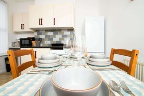 A dining area with a table set for four, white cabinets, a tiled backsplash, and a white refrigerator. - Cosy 2BR Flat Near Anfield & Goodison, Liverpool (Liverpool)