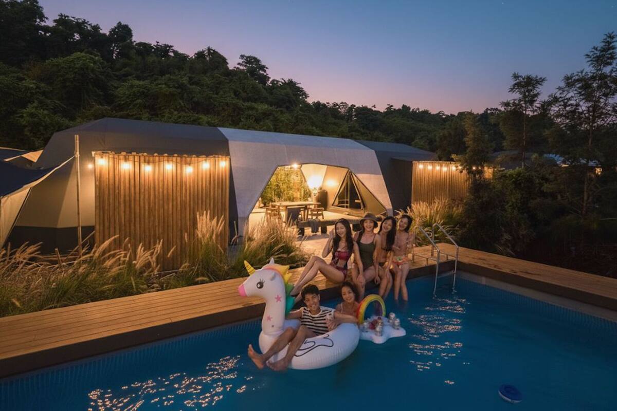 A modern tented accommodation with a pool area, surrounded by lush greenery.