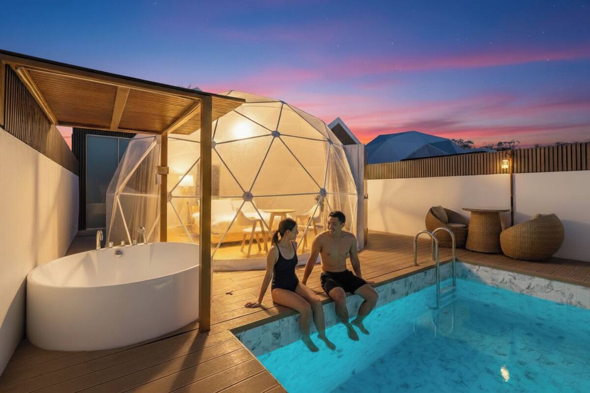 A couple sitting by a pool with a geodesic dome structure and a hot tub.