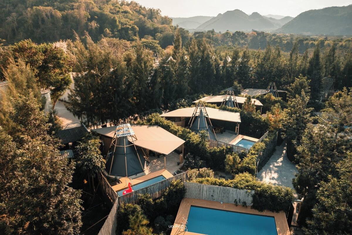 A resort with multiple yurts, a swimming pool, and a forested backdrop.