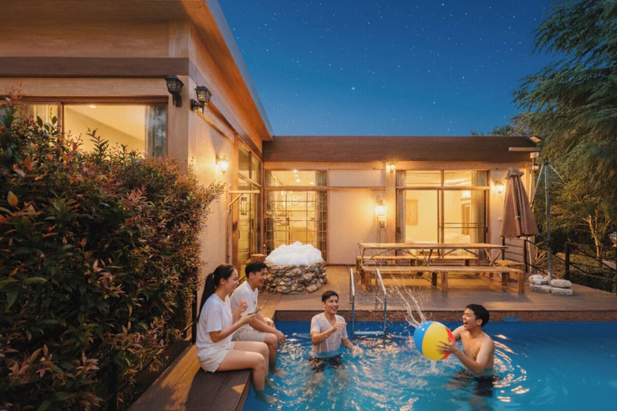 A poolside area with a wooden deck, a stone bench, and a water feature.