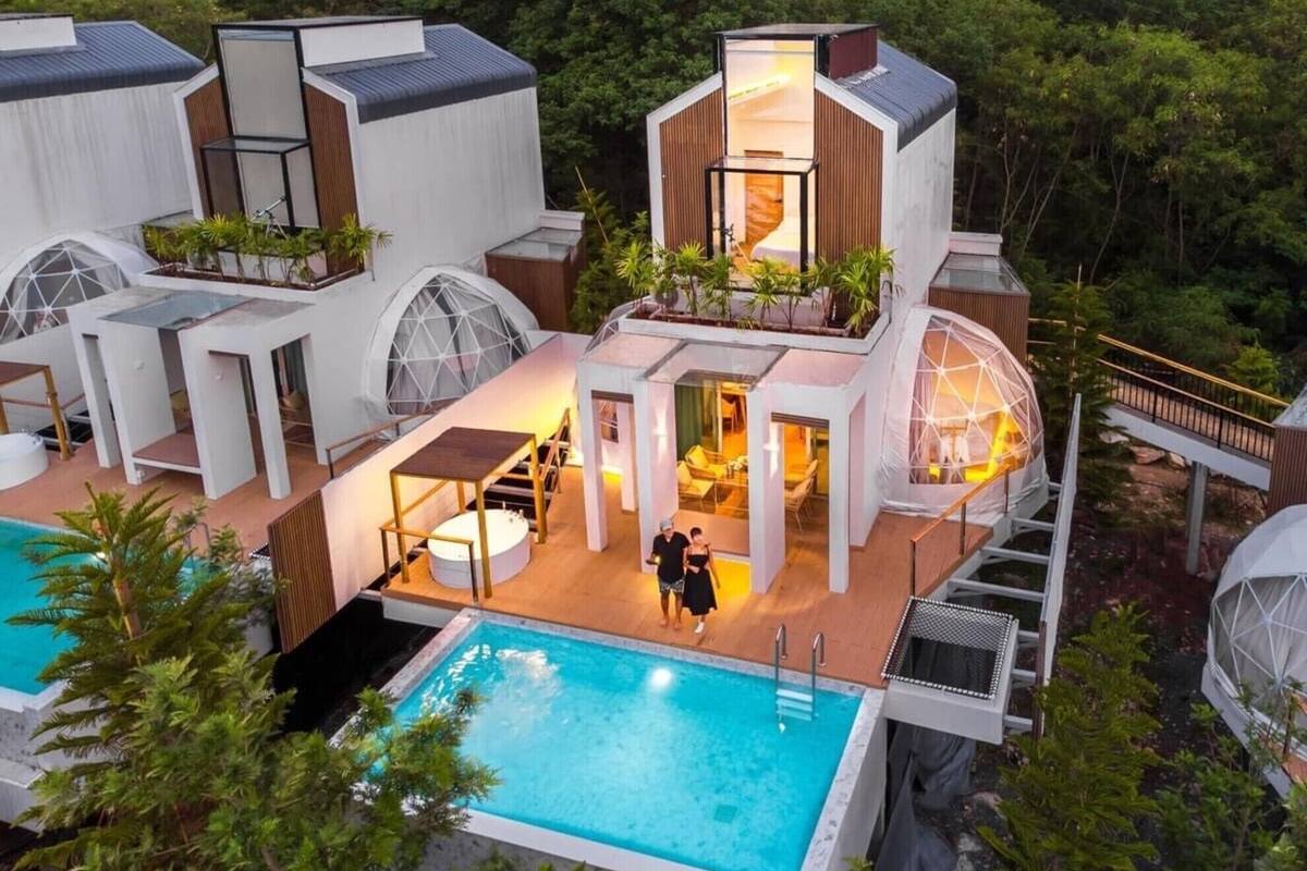 A modern multi-story house with a swimming pool, outdoor seating, and a glass greenhouse structure.