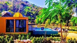 A modern building with a pool, surrounded by lush greenery and a mountain backdrop. - TheX10 PrivatePoolVilla & ResortKhaoYai (Pak Chong)