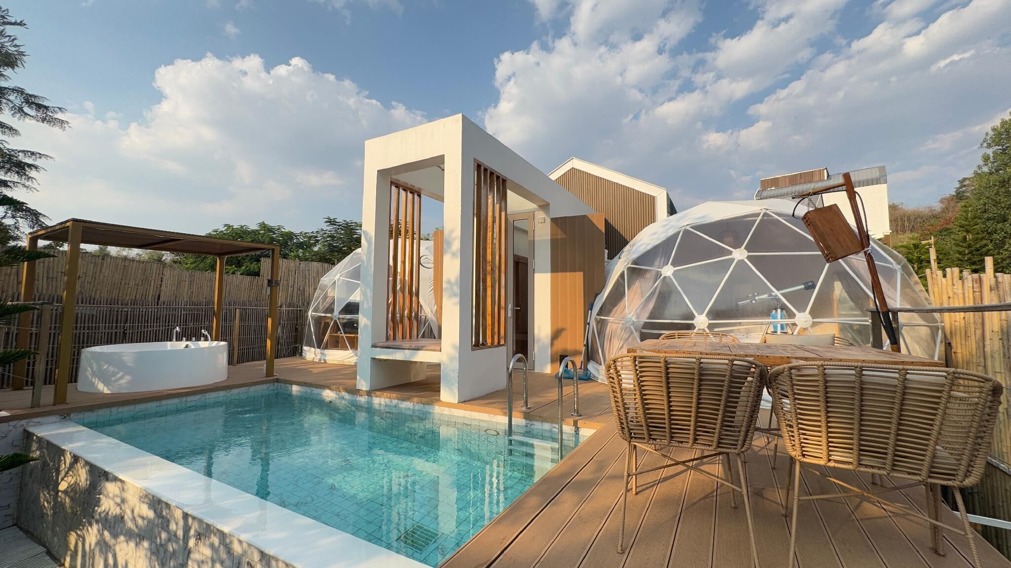 A modern outdoor pool area with a clear pool, wooden deck, and two large geodesic domes.