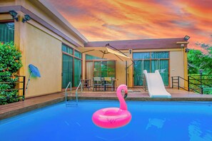 A swimming pool with a pink flamingo float, a slide, and a patio area with a table and chairs. - TheX10 PrivatePoolVilla & ResortKhaoYai (Pak Chong)