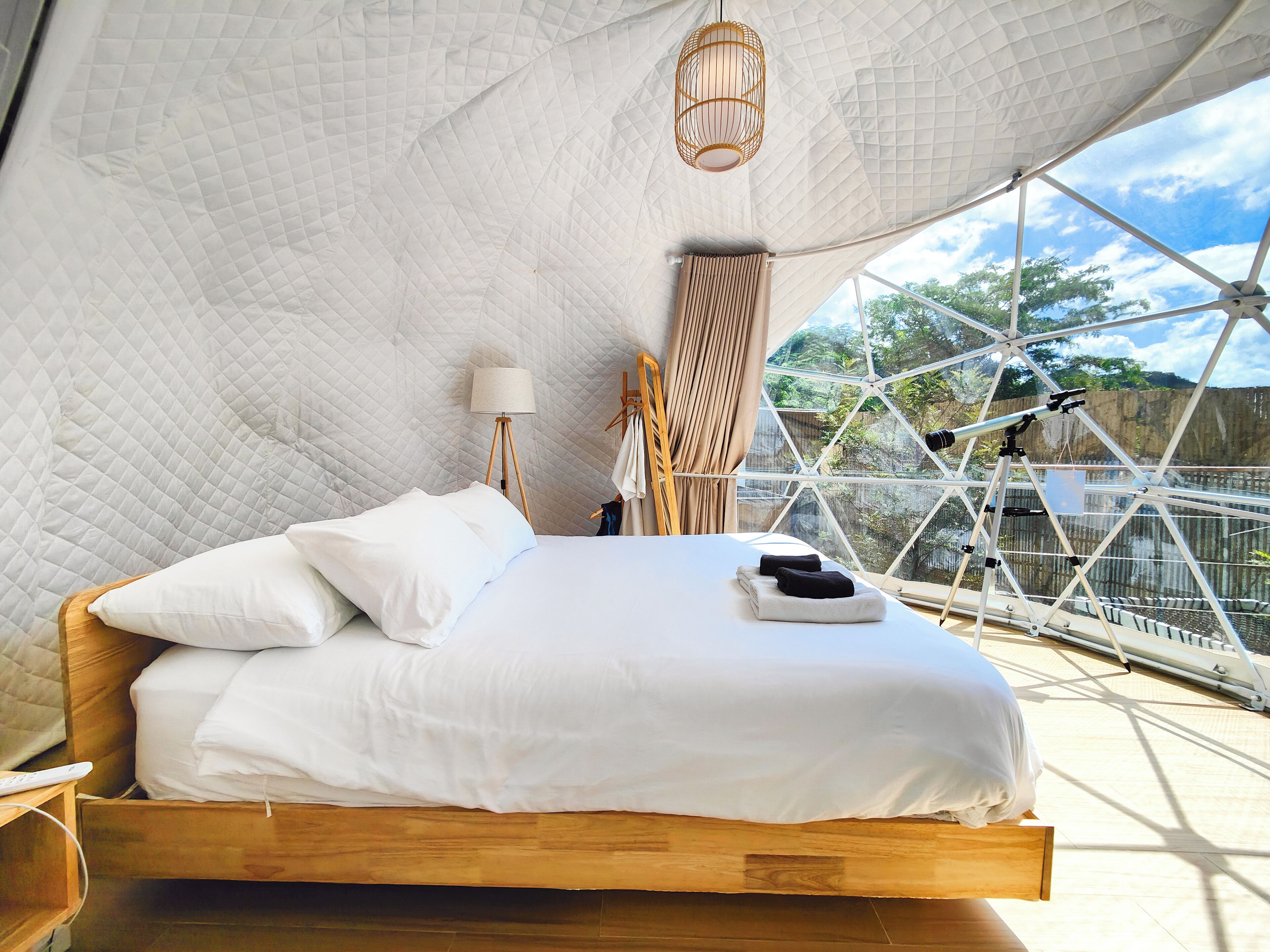 A bed in a geodesic dome room with a view of trees and a telescope.