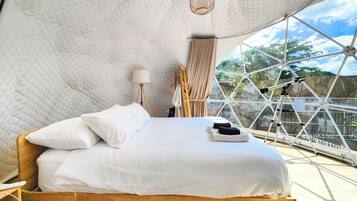 A bed in a geodesic dome room with a view of trees and a telescope.