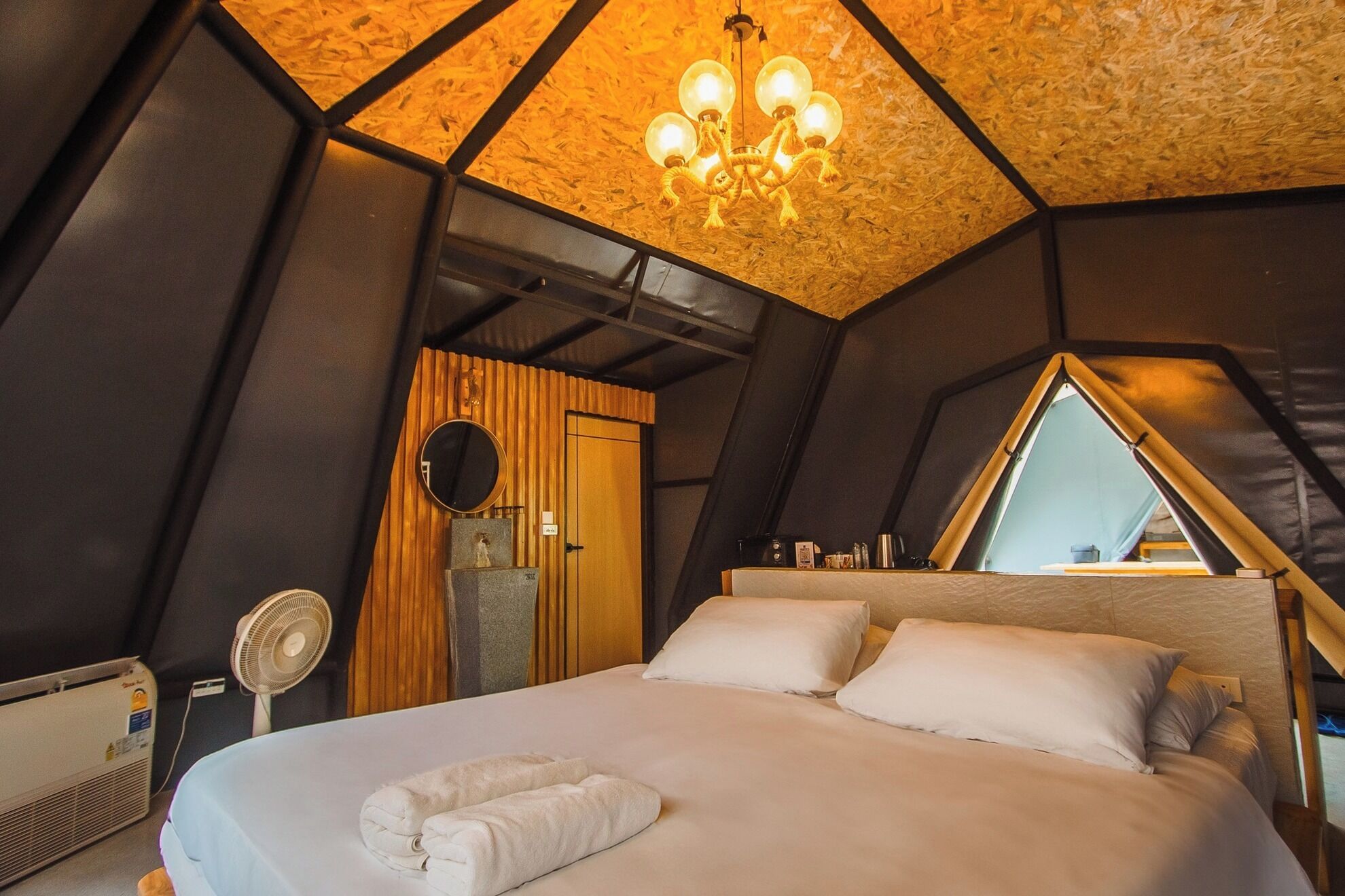A bedroom with a bed, a mirror, a fan, and a chandelier.