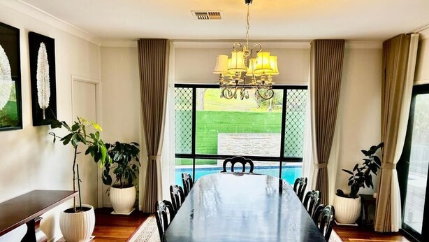 Un comedor con una larga mesa, sillas, un candelabro, plantas en macetas y vista a una piscina.