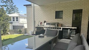 Un patio exterior con una mesa de vidrio, mobiliario de mimbre y una parrilla integrada.