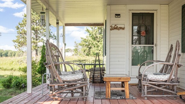 Une véranda avec deux fauteuils à bascule et une petite table, une pancarte de bienvenue et une vue sur le paysage environnant.
