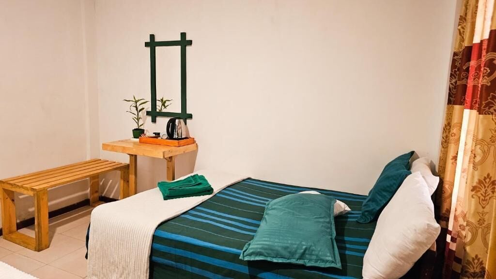 A bedroom with a bed, a wooden bench, a small table with a plant, and a mirror on the wall.