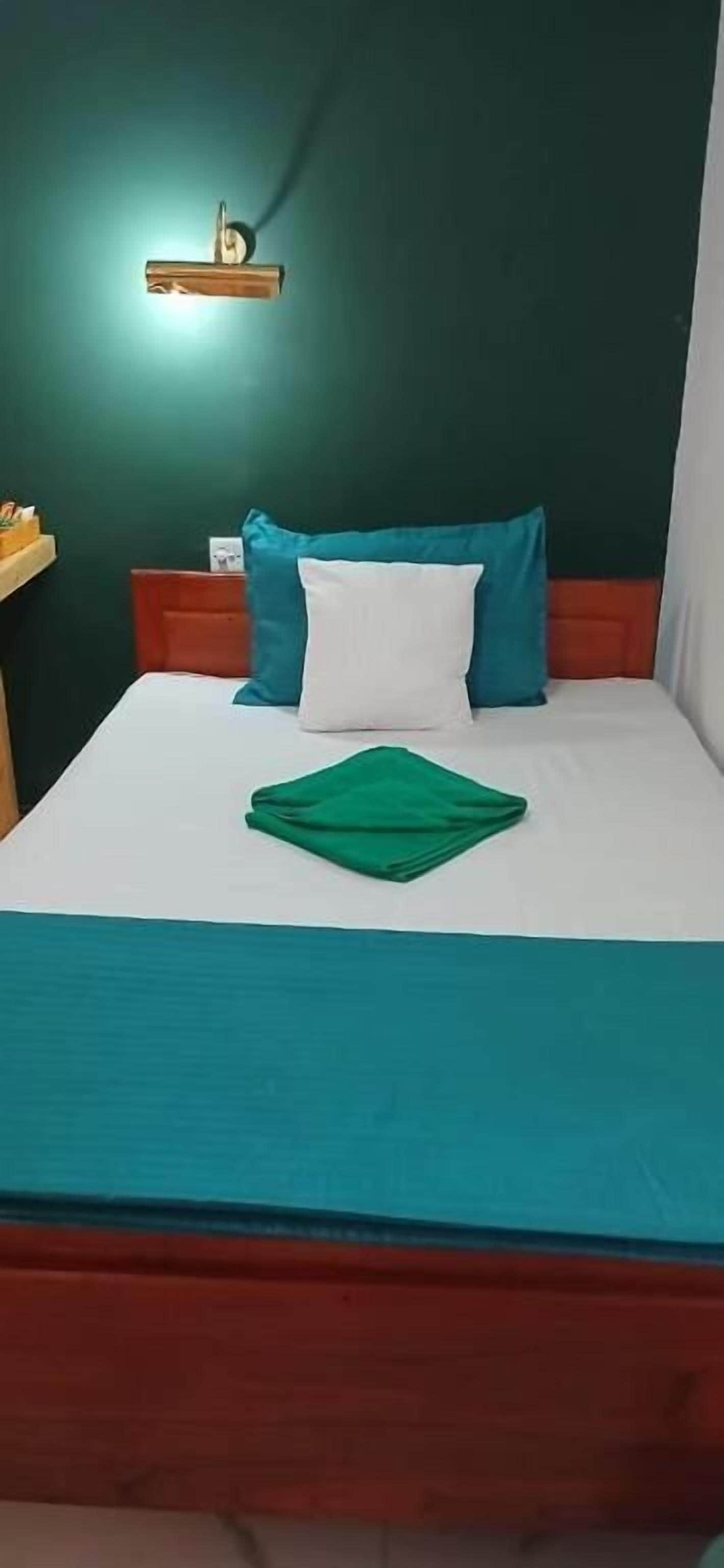 A bed with a white and teal bedspread, a green towel, and two pillows (one teal, one white).