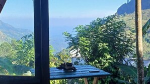 A view from a window overlooking a lush landscape with a table and a chair outside. - Misty Cabins Ella (Ella)