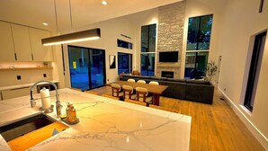 Una cocina moderna con una isla de mármol, comedor con sillas, horno empotrado y ventanas amplias.