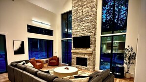 Una sala de estar moderna con un sofá modular grande, una chimenea de piedra y ventanas amplias con vista al cielo nocturno.
