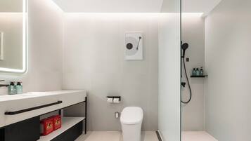 A modern bathroom with a toilet, a sink with a mirror, and a shower area.