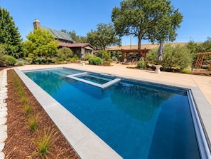 A rectangular swimming pool with a clear blue water surface, surrounded by a landscaped garden with various shrubs and trees. - Oaks & Madeira LuxEstate by Templeton Vaca Rentals (Paso Robles)