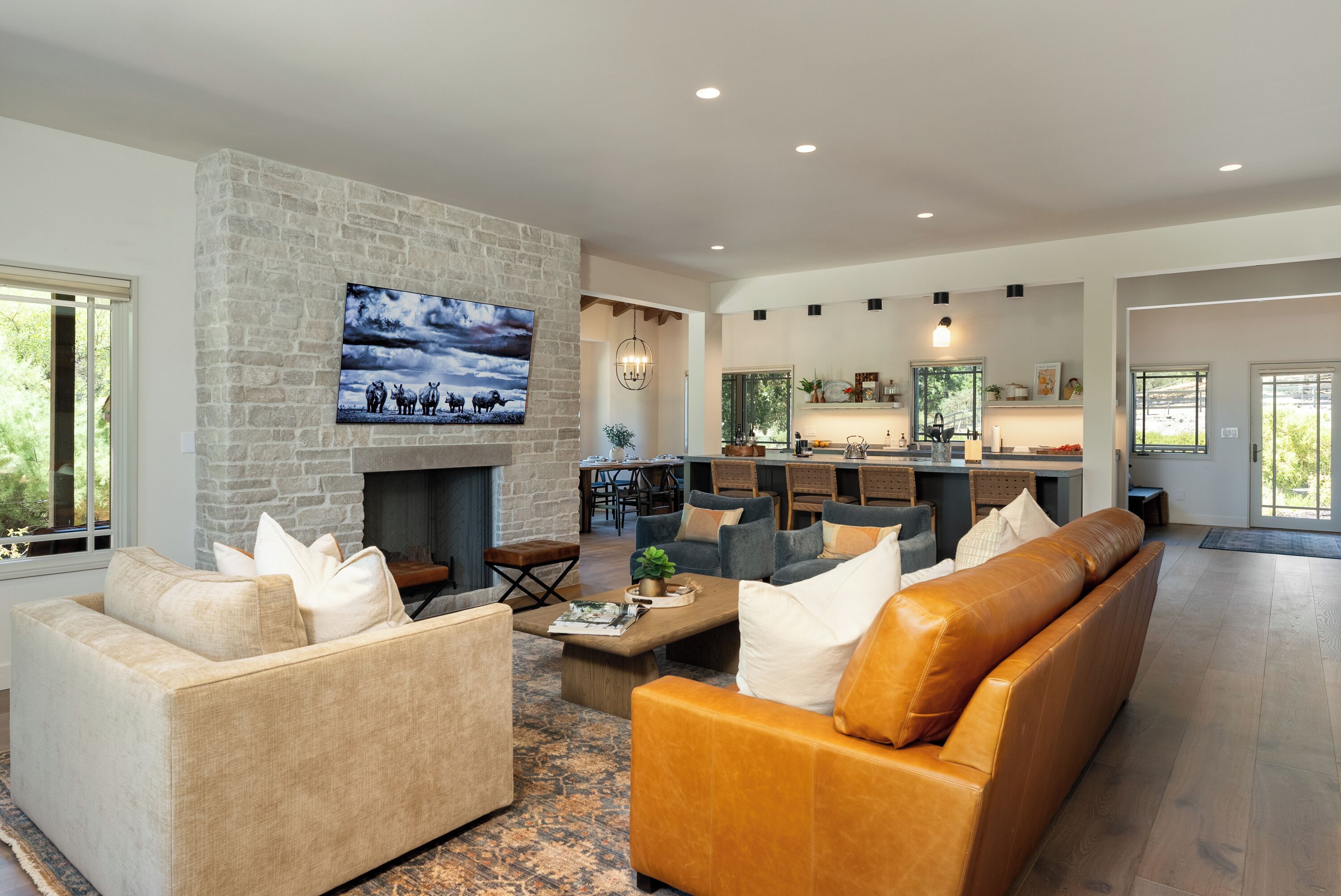 A spacious living room with a stone fireplace, comfortable seating, and a large TV mounted on the wall.
