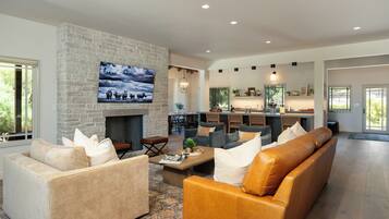 A spacious living room with a stone fireplace, comfortable seating, and a large TV mounted on the wall.