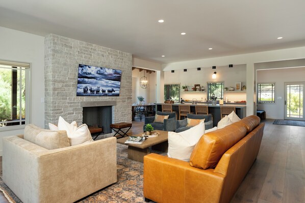 A spacious living room with a stone fireplace, comfortable seating, and a large TV mounted on the wall. - Oaks & Madeira—A Luxury Wine Escape in Paso Robles (Paso Robles)