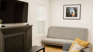 Un salon moderne avec un canapé gris, une table basse noire, une cheminée et un grand téléviseur à écran plat.