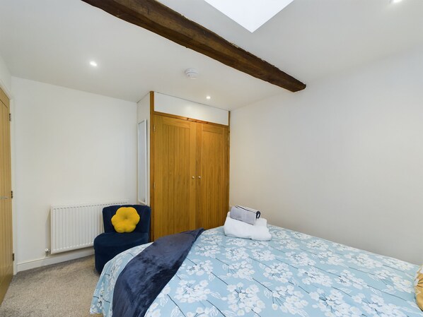 A bedroom with a skylight, a wooden wardrobe, a radiator, a bed with a floral bedspread, and a yellow cushion. - Woodman's Cottage, central Penrith with shops, bars, restaurants on doorstep, Ullswater 9mile (Penrith)