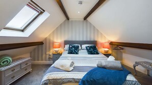 Een slaapkamer met een schuine plafond, dakraam, bed met behang, twee nachtlampjes en een klein tafeltje met lamp.