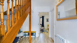 Een houten trap met een leuning, een hal met een radiator, en een deur die naar een andere kamer leidt.