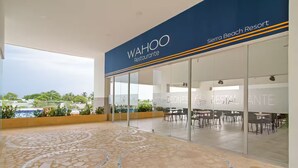 A WAHOO restaurant at Sierra Beach Resort with a glass facade, outdoor seating, and a view of the pool and greenery.