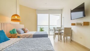 A hotel room with two beds, a TV, a balcony with a view, and a dining area with chairs.