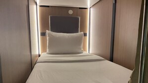 Ein gemütliches, gut beleuchtetes Schlafzimmer mit einem Einzelbett, einem Kopfteil und einem kleinen Nachttisch.