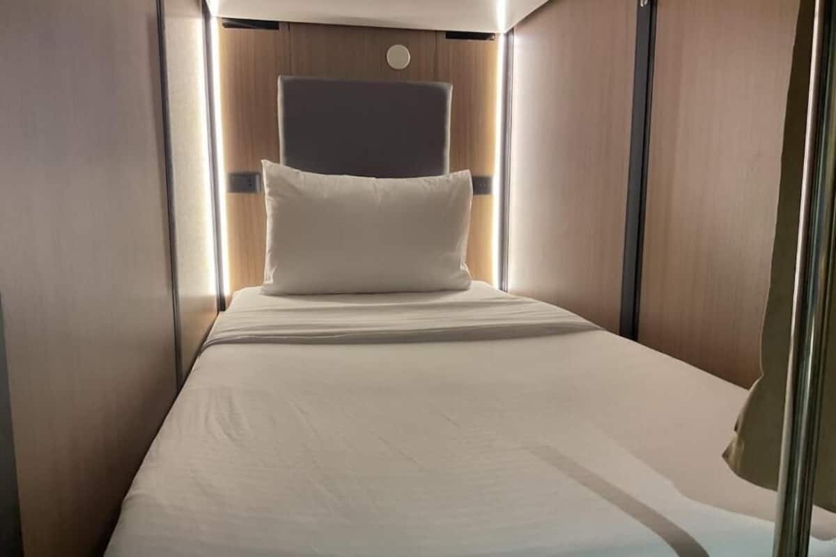 A compact, well-lit bedroom with a single bed, a headboard, and a small bedside table.