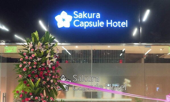 The exterior of Sakura Capsule Hotel with a neon sign and a large floral arrangement in front. - Sakura Capsule Hotel Cebu (Lapu-Lapu)