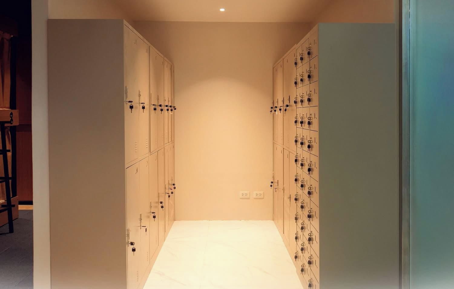A corridor with lockers on both sides, a white floor, and a ceiling light.