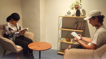 Una habitación con dos personas sentadas en sillas, una pequeña mesa redonda y una estantería con libros y adornos.