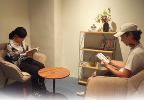 A room with two people seated on chairs, a small round table, and a bookshelf with books and decorative items. - Sakura Capsule Hotel Cebu (Lapu-Lapu)