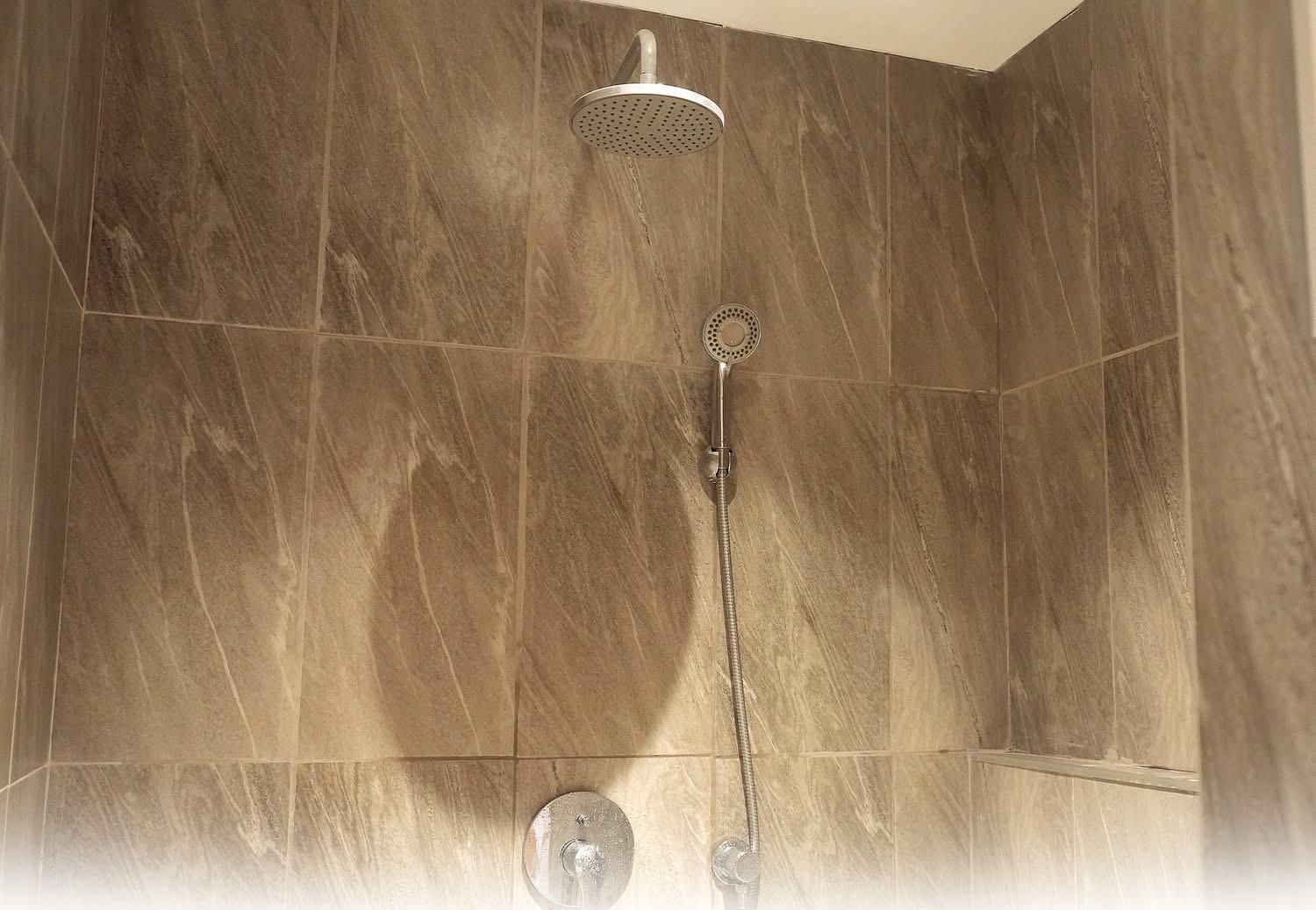 Ducha con cabezal de ducha manual y cabezal de ducha de lluvia empotrado en la pared, en un baño con baldosas similares al mármol.