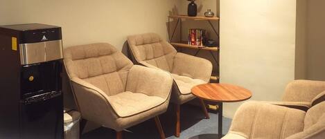 A seating area with two armchairs and a small round table, a coffee machine, and a bookshelf with books and a vase of flowers.