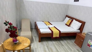 Een kleine, verzorgde kamer met een bed, een stoel, een tafel en een koelkast.