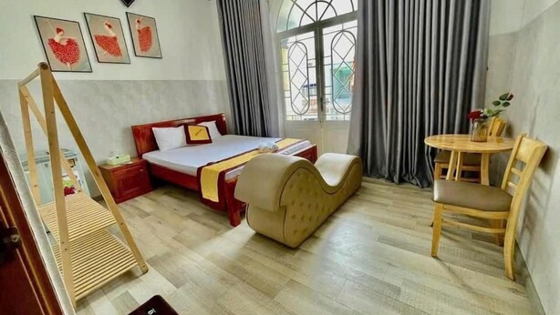 Een hotelkamer met een bed, een houten stoel, een klein tafeltje en een raam met gordijnen.