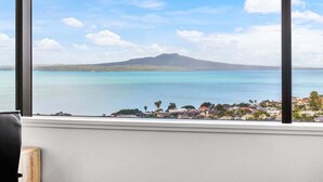 A view from a window overlooking a coastal area with a mountain in the distance. - Awesome 1BR Apartment Kitchen Tennis Gym Hot Tub (Auckland)