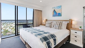 A hotel room with a large bed, a city view, a painting on the wall, and a nightstand with a lamp. - Awesome 1BR Apartment Kitchen Tennis Gym Hot Tub (Auckland)
