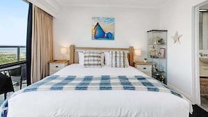 A hotel room with a large bed, a painting above the bed, a nightstand, a lamp, a star decoration, and a view of the outside. - Awesome 1BR Apartment Kitchen Tennis Gym Hot Tub (Auckland)