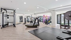 A modern gym with cardio equipment, weight machines, and a large mirror. - Awesome 1BR Apartment Kitchen Tennis Gym Hot Tub (Auckland)