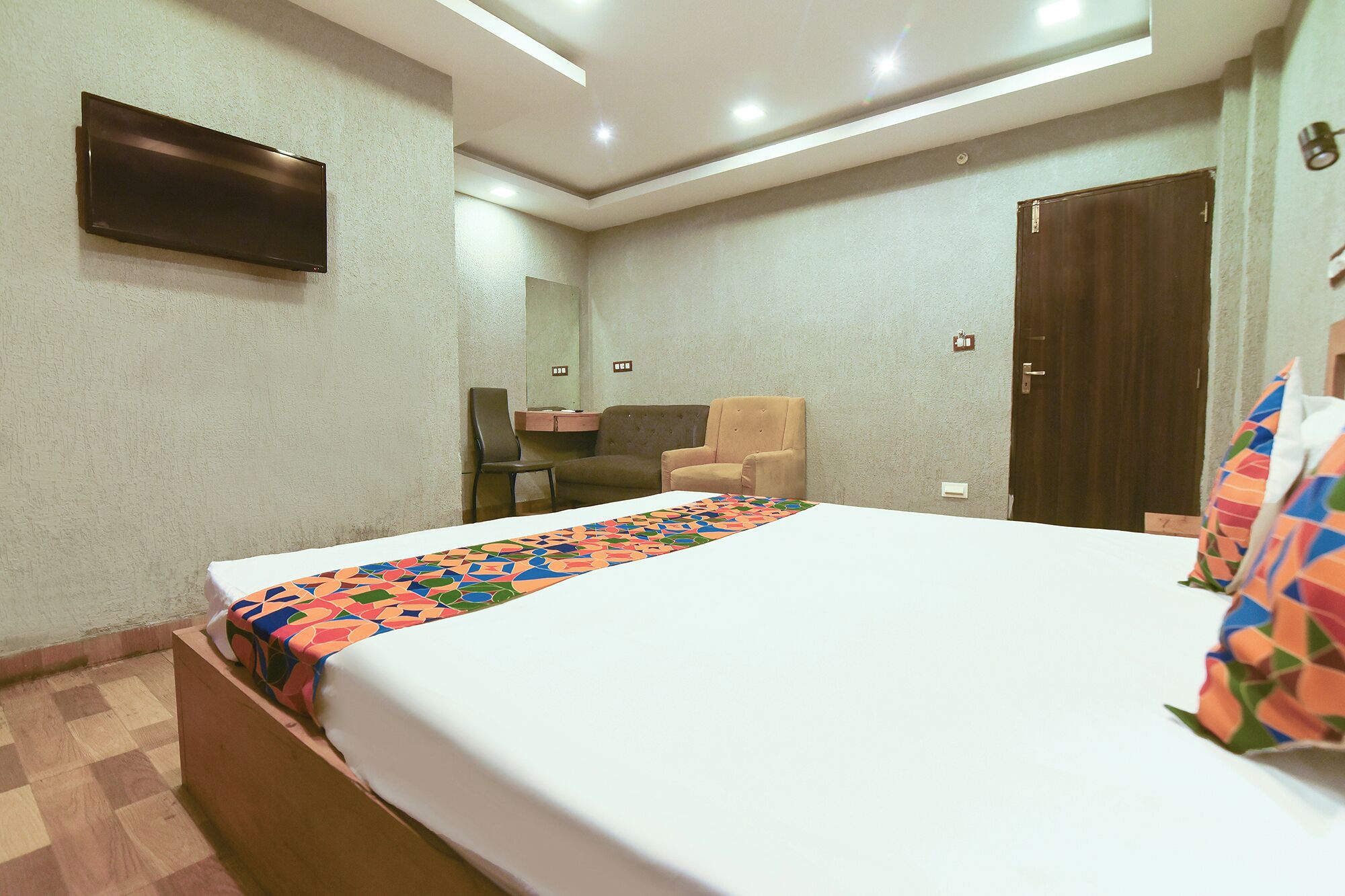 A hotel room with a large bed, a desk, a chair, and a wardrobe.