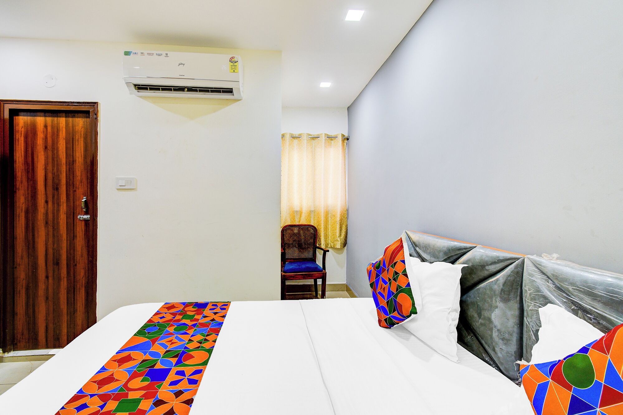 Una habitación de hotel con cama, una silla, aire acondicionado y una puerta.
