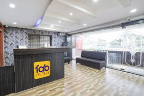 A hotel reception area with a modern design, including a reception desk, a sofa, and a large window offering a view of the outside. - Fabhotel Millennium Suites (Anekal)