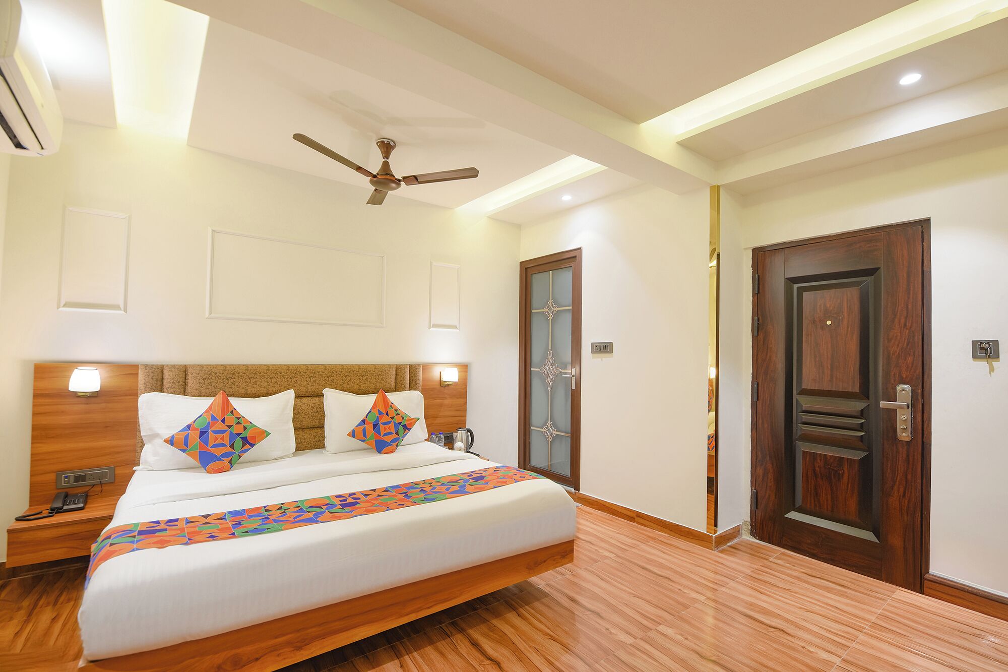 A hotel room with a large bed, a ceiling fan, a wooden headboard, and a wooden door.